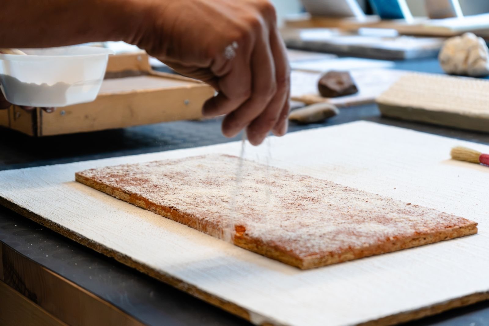 Mano che spolvera polvere minerale su un pannello durante la lavorazione